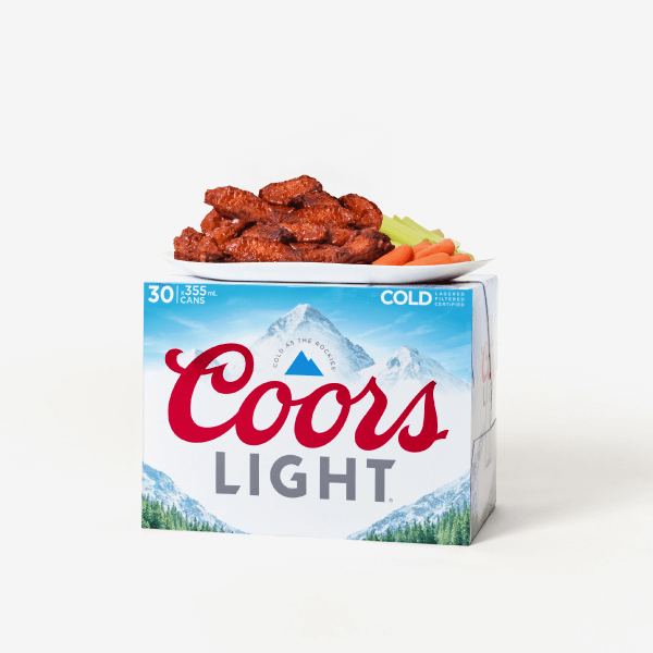 Plate of chicken wings with celery and carrots placed on top of a Coors Light beer case against a white background.