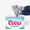 Person wearing jeans and sneakers with feet resting on a Coors Light beer case against a white background.